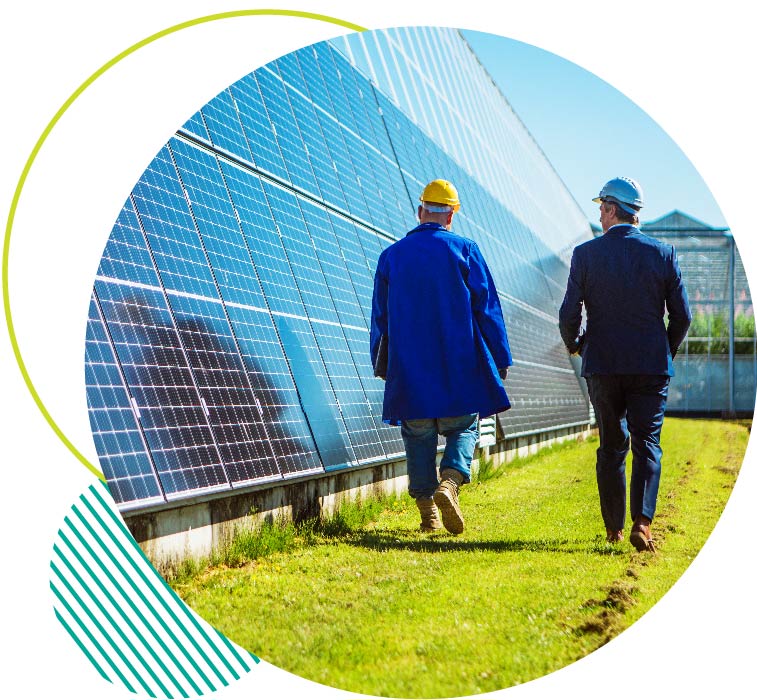 Two people in suits and hardhats walking next to solar panels